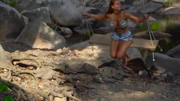 熱帯雨林でのスイングに笑顔の女性。ロッキー川岸の揺れを楽しんで幸せな女. — ストック動画