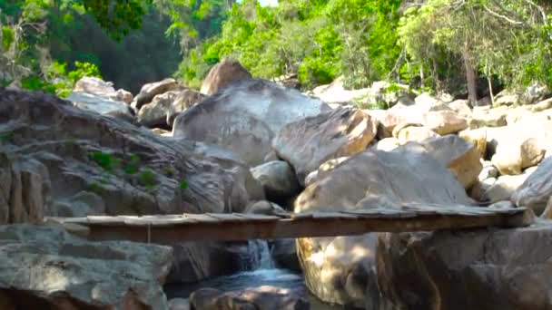 Pojke med ryggsäck gå på träbro över snabba floden medan klättra i bergen. Pojke turist gå på hängbro bakgrund berg och stony river i djungeln skogen. — Stockvideo