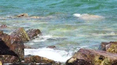 Taşlı kumsalda sıçramasına dalgalar deniz. Dalgalar üzerinde kayalık plaj kırma. Mavi deniz suyu ve büyük taşlar arka plan.