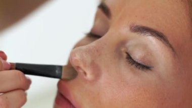 Visagiste kozmetik ile yüz makyaj model üzerinde uygulanan sesi krem fırça. Closeup sanatçı güzellik salonu genç kadın için makyaj makyaj.