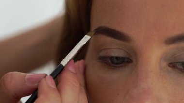 Kadar genç kadın yüz makyaj kaşları sırasında kapatın. Makyaj sanatçı resim kaşlar yüz makyaj yaparken. Güzellik ve moda endüstrisi kavramı.