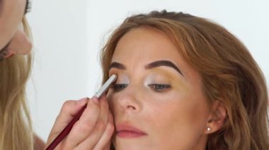 Yüz makyaj model uygulama makyaj güzellik Studio kapatın. Yapmak yapıyor Visagiste yukarı gözler güzel kadına kozmetik fırça ile. Güzellik ve moda endüstrisi.