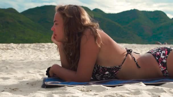 녹색 산 배경에 여름 해변에서 일광욕 하는 젊은 여자. 모래 해변에서 선탠 하는 비키니 태양에서 아름 다운 여자. — 비디오