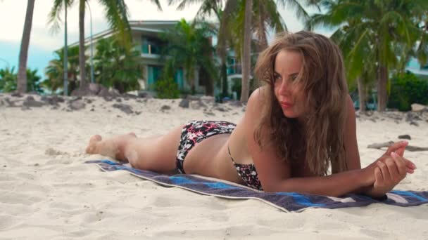 Mujer joven en bikini tomando el sol en la playa de verano en el fondo de villa de lujo. Hermosa mujer bronceado en la toalla de playa . — Vídeos de Stock