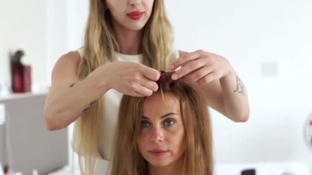 Enfrente a jovem enquanto cria penteado no estúdio de beleza. Cabeleireiro fazendo penteado de moda para mulher com cabelo castanho longo. Retrato mulher bonita no salão de cabeleireiro . — Vídeo de Stock