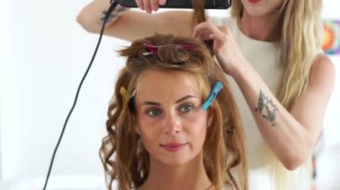 Curling saç demir güzellik Studio'yu kullanarak süre genç kadın yüz. Kuaför saç saç maşa ile güzel kadınla yapma kapatın. Güzellik ve saç şekillendirme kavramı