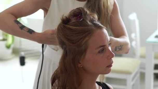 Парикмахер, используя щипцы для волос для кёрлинга, создает стильную прическу для молодой женщины в студии красоты. Парикмахер делает прическу с утюгом для длинноволосых женщин . — стоковое видео