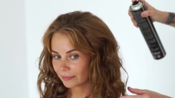 Portrait beautiful woman during creating curly hairstyle in hairdressing salon. Hairstylist using hairspray for fixing curling hair to fashion model. Hairdressing and hairstyling concept. — Stock Video