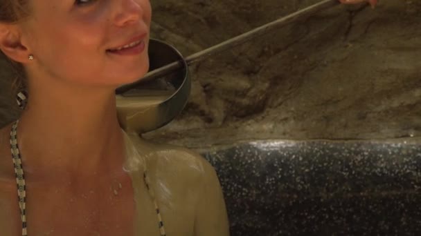 Smiling woman taking mud bath in spa center. Beautiful woman bathing in mud spa and pouring body from scoop. Wellness and healthy concept. Body care and skin care in spa procedures. — Stock Video