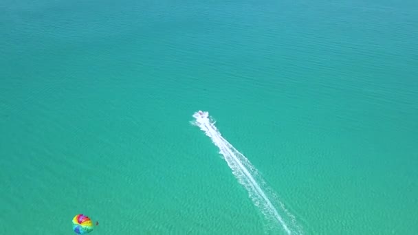 Парашют в голубом море с беспилотника. Парусный спорт летом и экстремальные развлечения во время отдыха на курортном пляже. Разноцветное крыло парашютиста, вытянутое на морской лодке с видом на море . — стоковое видео