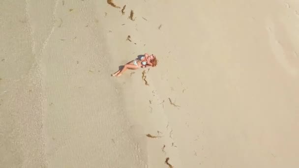 Schöne Frau im Bikini liegt auf Sand am Meer Strand Luftaufnahme. sexy Frau Bräune am Sommerstrand, Meereswellen und Sand Hintergrund. Mädchen von oben ruhen sich am Paradiesstrand aus. — Stockvideo