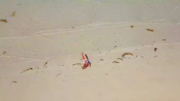 Junge Frau im Bikini im Sand am Strand von Droneview. glückliche Frau, die sich am Sommerstrand bräunt, Meereswellen und Sandhintergrund. Mädchen ruht und badet am Paradiesstrand. — Stockvideo