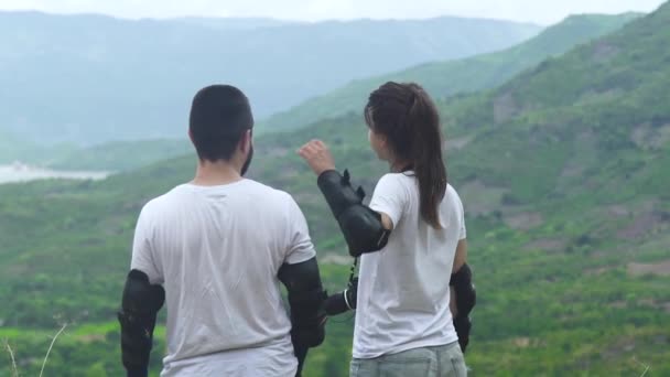 Pareja viajera hombre y mujer abrazándose en el borde de la montaña y mirando el valle verde y el bosque tropical. Gente turística de pie en la montaña vista trasera . — Vídeos de Stock