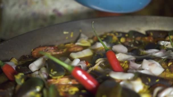 厨师烹调西班牙海鲜饭与红辣椒和新鲜海鲜在平底锅关闭。传统西班牙海鲜饭, 贻贝, 虾, 鱿鱼和蔬菜在平底锅. — 图库视频影像