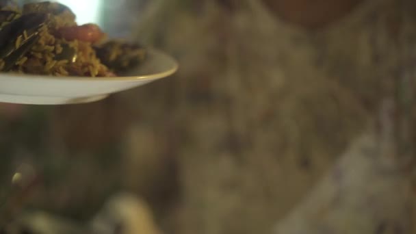 Homem com prato tradicional paella na mão preparado em restaurante espanhol. Homem segurando paella espanhola com frutos do mar frescos e legumes em pratos . — Vídeo de Stock