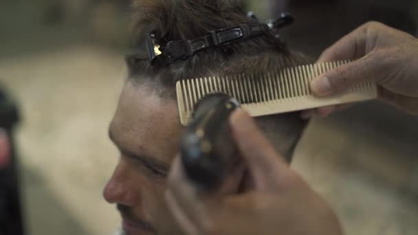 Peluquero haciendo corte de pelo masculino con afeitadora eléctrica y peine en la barbería. Primer plano de la peluquería masculina. Hombre cortarse el pelo con maquinilla de afeitar eléctrica en la peluquería. Peluquería masculina con trimmer . — Vídeos de Stock