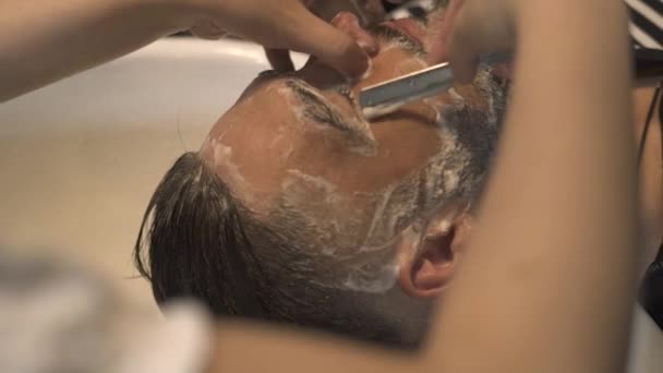 Afeitado peluquero con afeitadora recta al hombre barbudo en salón masculino. Cierre la barba de afeitar con afeitadora recta y espuma de jabón en la cara. Concepto de barbería. Barba masculina cuidado — Vídeos de Stock