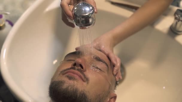 Peluquero lavando el cabello al hombre barbudo en el salón masculino. Peluquería mano lavar la cabeza masculina y la cara de la piel de cerca. Cliente en el salón de peluquería. Peluquero lavando la cara y el pelo al hombre hipster . — Vídeo de stock