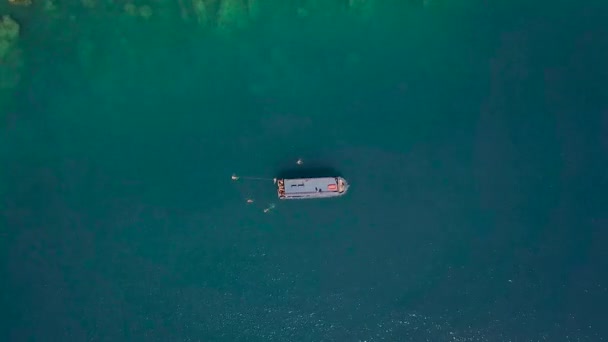 निळ्या समुद्राच्या लेगूनमध्ये जहाज आणि क्रिस्टल स्पष्ट पाण्याच्या वरच्या दृश्यात पोहणारे लोक. ड्रोन समुद्रात प्रवास करणारी बोट आणि लोक निळ्या पाण्यात आंघोळ करतात. हवाई लँडस्केप . — स्टॉक व्हिडिओ