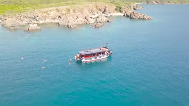 Drone voando sobre barco à vela e as pessoas que tomam banho em água do mar azul. Paisagem aérea turística nadando no mar e penhasco rochoso na costa. Top vista navio navegando na lagoa azul . — Vídeo de Stock