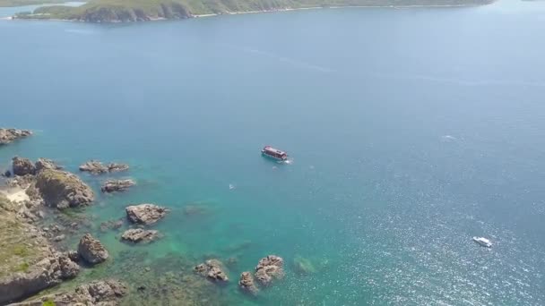 Boot, das im blauen Meerwasser segelt und Menschen, die in klarem Wasser schwimmen. Drohnenfliegendes Segelboot in Meeresbucht und Bergklippe an Land. von oben Blaue Lagune. — Stockvideo