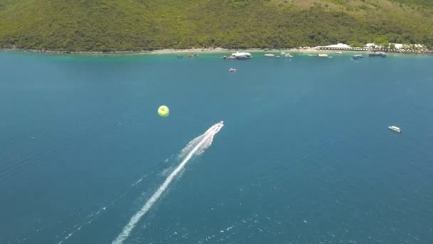 Parasailing i blå havet bay drönarvy. Flygfoto segelbåt med skärmflygning i turkosa havet. Vackra landskap blå lagunen och resort beach på ön. — Stockvideo