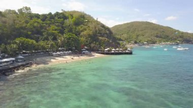 Yaz plaj resort ve mavi hava manzara su. Kumsalda dinlenme ve defne deniz yüzme insanlar. Dron görünümü kumlu plaj tropikal ada ve yeşil tepe manzara.