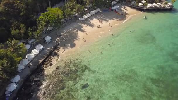 Zomer strand aan de kust met transparante water luchtfoto landschap. Mensen rusten op resort strand en zwemmen in zee baai. Drone uitzicht zandstrand strand op groene eiland landschap. — Stockvideo