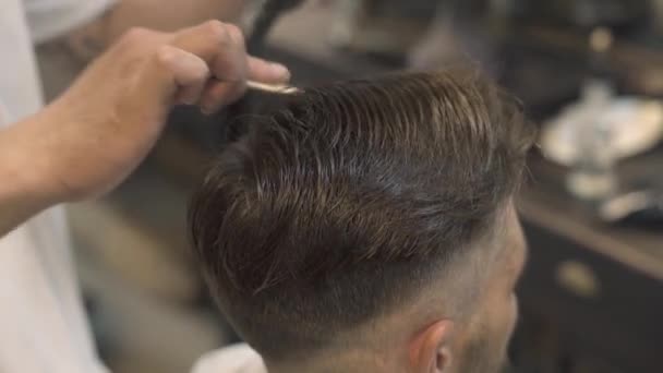Barbeiro fazendo penteado hipster com secador no salão masculino. Cabelo masculino penteando e secando na barbearia. Cabeleireiro usando secador para cabelo styling. Penteado de homem de moda no salão . — Vídeo de Stock