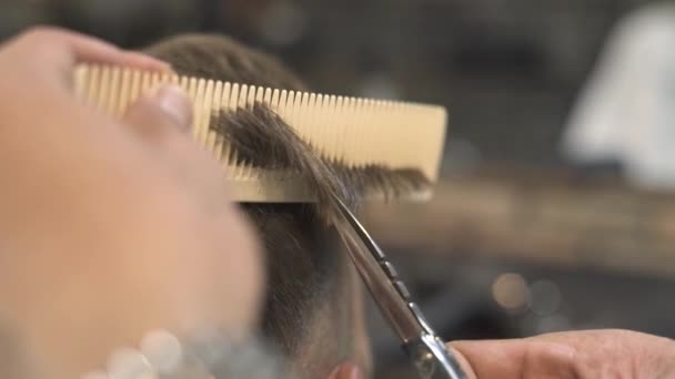 Barber cutting hair with scissors and comb in male salon. Close up hipster haircut with hair scissors in barbershop. Professional male hairstyle in hairdressing salon.
