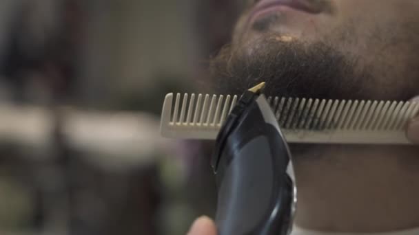 Barbero barba de afeitar con maquinilla de afeitar eléctrica y peine en salón masculino. Peluquero macho recortando la barba con afeitadora de cerca. afeitado profesional barbudo hombre . — Vídeos de Stock
