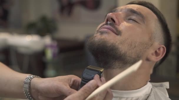 Barber shaving beard with electric razor to hipster man in male salon. Male barber trimming beard with electricshaver. Stylish shaving bearded man. — Stock Video