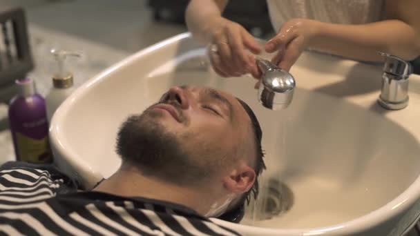 Tvář při mytí vlasy a hlavu v kadeřnictví salon zblízka. Kadeřník rukou umýt mužské hlavy v mužské salonu. Mužské holičství salon. Mytí vlasů mladíka v holičství. — Stock video