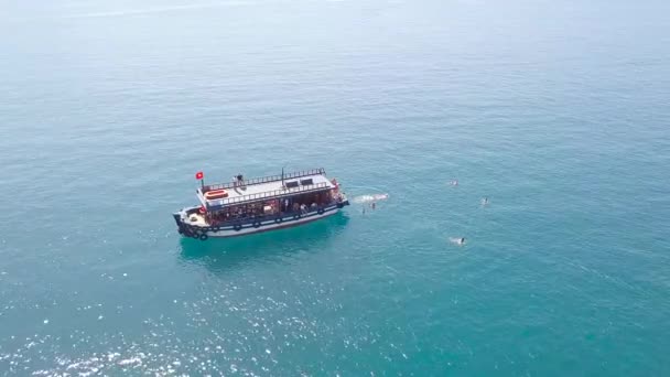 Luchtfoto shot blauwe zee lagune met zeilschip en zwemmen mensen. Drone weergave mensen zwemmen rond boot varen in turquoise zeewater. — Stockvideo
