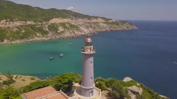 Drone uitzicht zee vuurtoren op berg klif en zeilen schepen. Luchtfoto landschap vuurtoren op groene berg en boot varen in turquoise zee. — Stockvideo