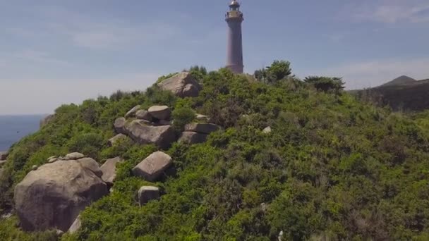 Zee vuurtoren op groene bergen en rotsenstranden drone weergave. Luchtfoto vuurtoren op berg rots en landschap turquoise zee. — Stockvideo