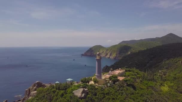 Vue sur drone phare sur les montagnes verdoyantes et la mer bleue sur l'horizon clair. Vue aérienne phare de mer sur falaise de montagne et ciel bleu paysage . — Video