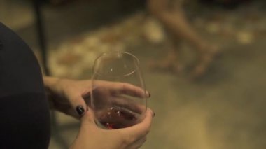 Kırmızı şarap tutan eller restoranda cam. Kırmızı bardağı ve siyah giysiler içinde restoran yürüyen kadın ile kapatmak.