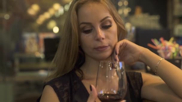 Young woman holding in hand red wine glass and smelling aroma in restaurant. Woman tasting and drinking red wine at event party in cafe. — Stock Video