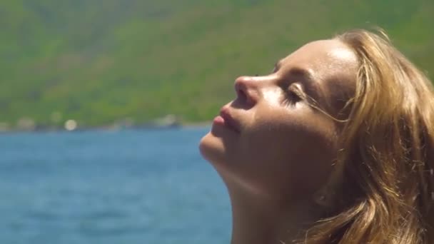 Faccia la bella donna che prende il sole a giorno soleggiato su paesaggio di mare. Ritratto da vicino giovane donna con capelli dorati e marroni che prende il sole sulla spiaggia del mare . — Video Stock