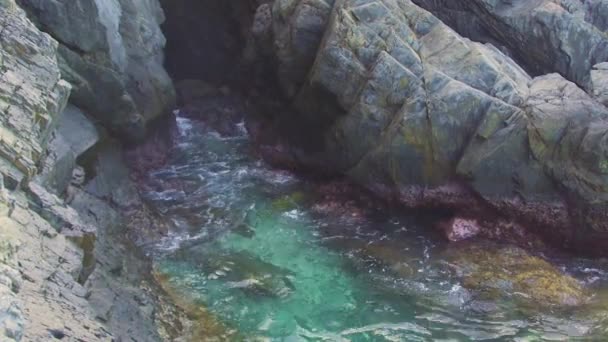 Onde d'acqua di mare azzurro che schizzano sulla scogliera rocciosa. Onde che si infrangono sulla montagna scogliera. Blu acqua di mare e grandi pietre di sfondo . — Video Stock