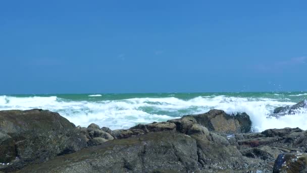 Onde marine che schizzano sulla spiaggia rocciosa su un cielo azzurro. Chiudi onde d'acqua che si infrangono sulla costa rocciosa nell'oceano. Blu mare e cielo sfondo . — Video Stock