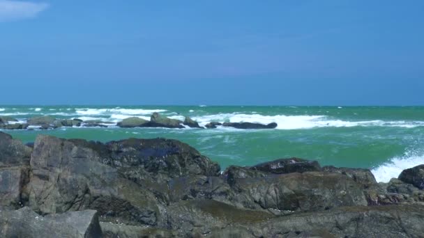 Mar tormentoso y olas de agua salpicando en la playa rocosa en el paisaje del cielo azul. Olas de agua rompiendo en costa pedregosa en el océano. Mar azul aplastando un acantilado rocoso en el fondo del cielo . — Vídeos de Stock