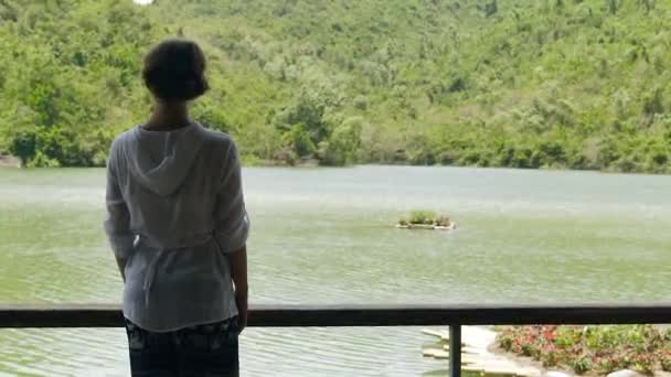 Jovem mulher de pé no fundo do rio e montanha coberto floresta verde. Menina assistindo no rio e paisagem de montanha verde, vista traseira . — Vídeo de Stock