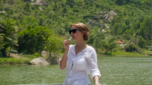 Porträt einer jungen Frau, die am Ufer des Flusses und im grünen Hintergrund der Berge Zigarette raucht. Mädchen raucht am Seeufer und bergige grüne Waldlandschaft. — Stockvideo