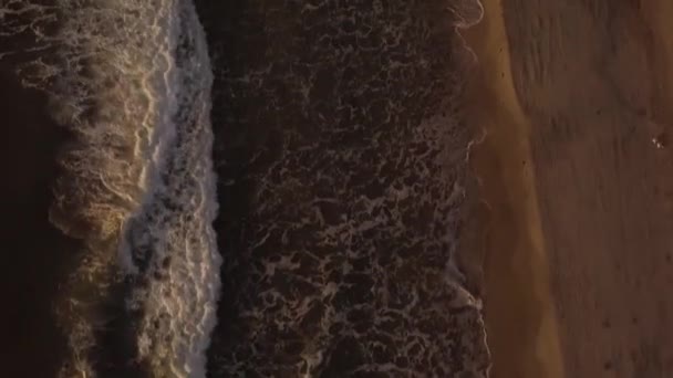 Drone volando sobre olas de agua de mar con espuma blanca salpicando en la orilla arenosa. Vista aérea de las olas del océano en la playa de la noche. Vista superior del mar surf en la playa de la mañana . — Vídeos de Stock