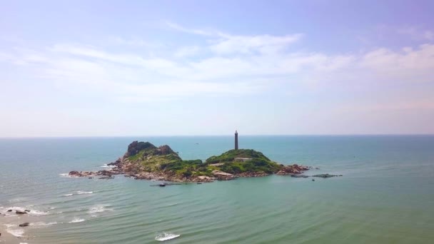 Phare de vue aérienne sur une île rocheuse dans un paysage marin bleu. Vue sur drone maison lumineuse sur falaise dans l'océan sur fond de ciel bleu . — Video