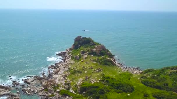 Sziklás sziklán a zöld sziget, kék tenger és a vitorlás hajó a skyline antenna tájkép. Drone nézet cliff sziklás partján, zöld szigeten az óceán és a hajó kifutását a láthatáron. — Stock videók