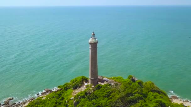 Phare sur île verte dans un paysage aérien de mer turquoise. Vue sur drone haut phare sur une île rocheuse dans un paysage bleu océan . — Video