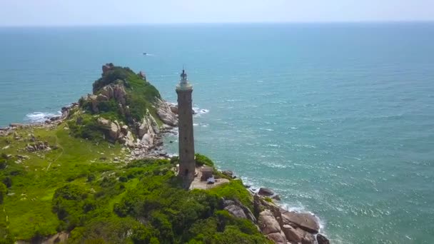 Sea light house on green shore and blue water aerial landscape. Drone view lighthouse on rocky island in ocean and blue blue water background. — Stock Video